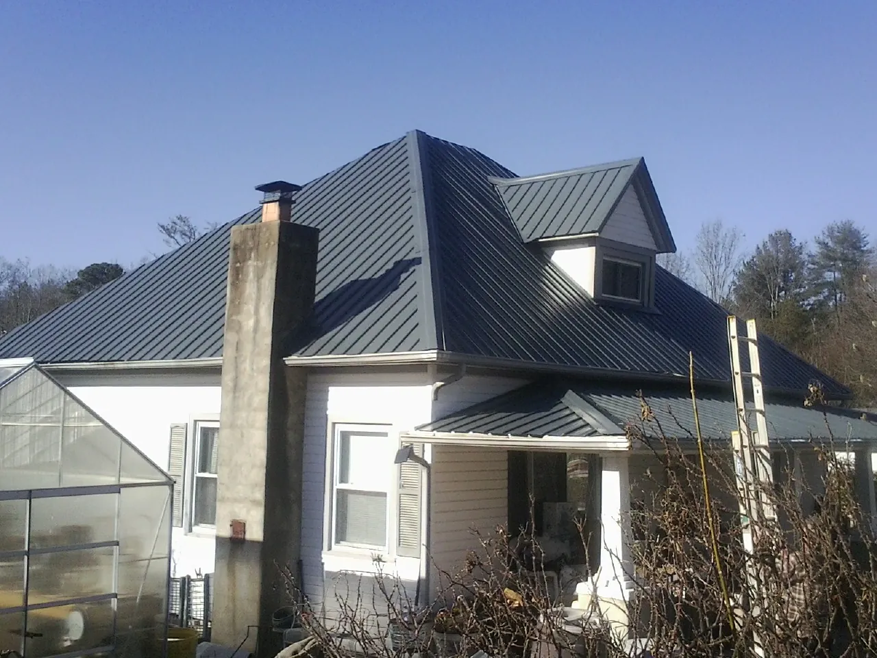 Dark blue standing seam metal roof on a white farmhouse with dormer — Slate & Tile Roof Repair by Roofing Brothers in New Hudson