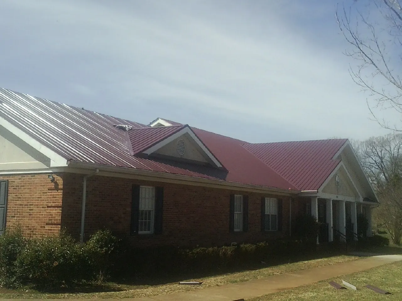 Red metal roof with gabled entries on a long brick building, from a Hail Damage Roof Repair job in New Hudson