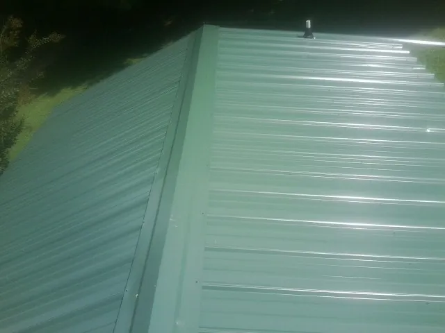 New green metal panels meeting at the ridge of a roof — Flat Roof Repair work by our crew in New Hudson