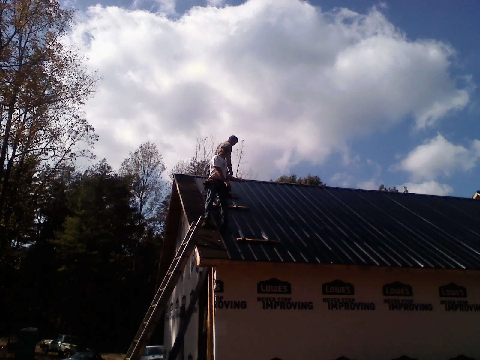 Roofer fastening dark metal panels high against a cloudy sky, from a Roof Inspection job in New Hudson