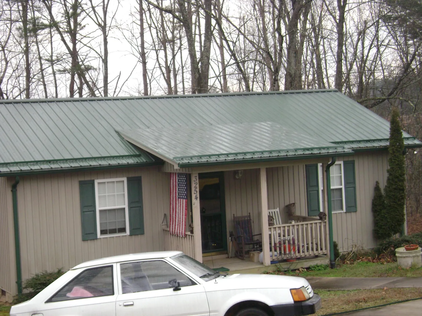 Green metal roof and front porch on a tan sided cottage in New Hudson
