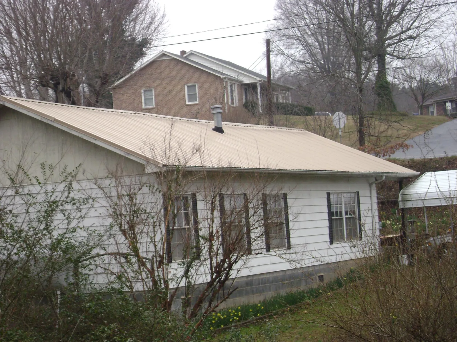 Tan metal roof on a white sided house set into a hillside — Commercial Roofing by Roofing Brothers in New Hudson