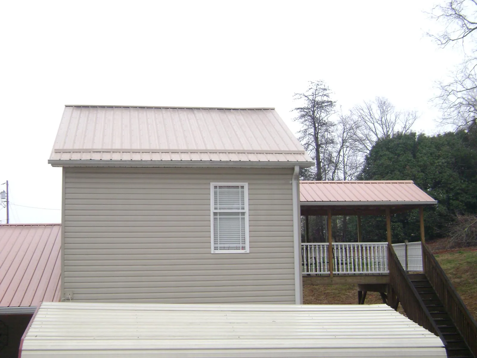 Tan metal roofs on a two story addition and attached porch, from a Roof Replacement job in New Hudson